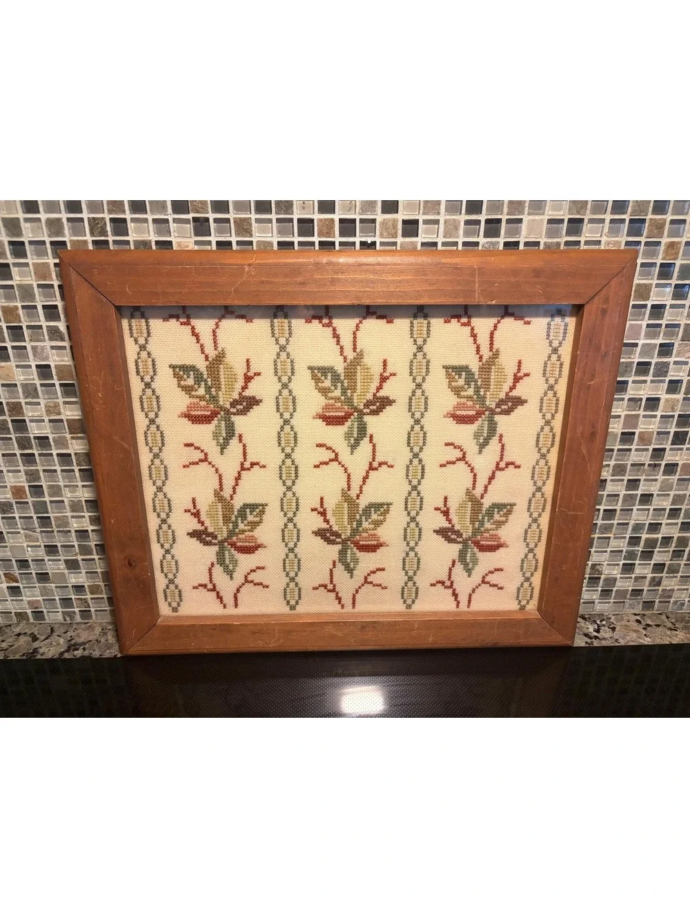 This is a vintage framed botanical cross-stitch or needlepoint textile panel.